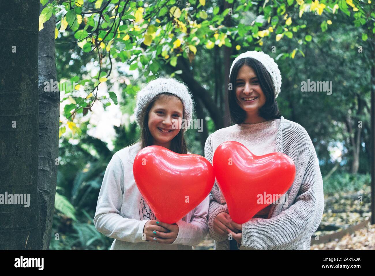 Smiling girls holding heart balloon by trees Stock Photo