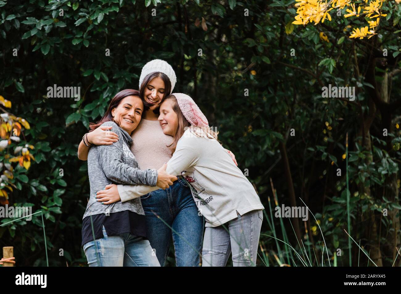 Mother and daughters embracing by trees Stock Photo