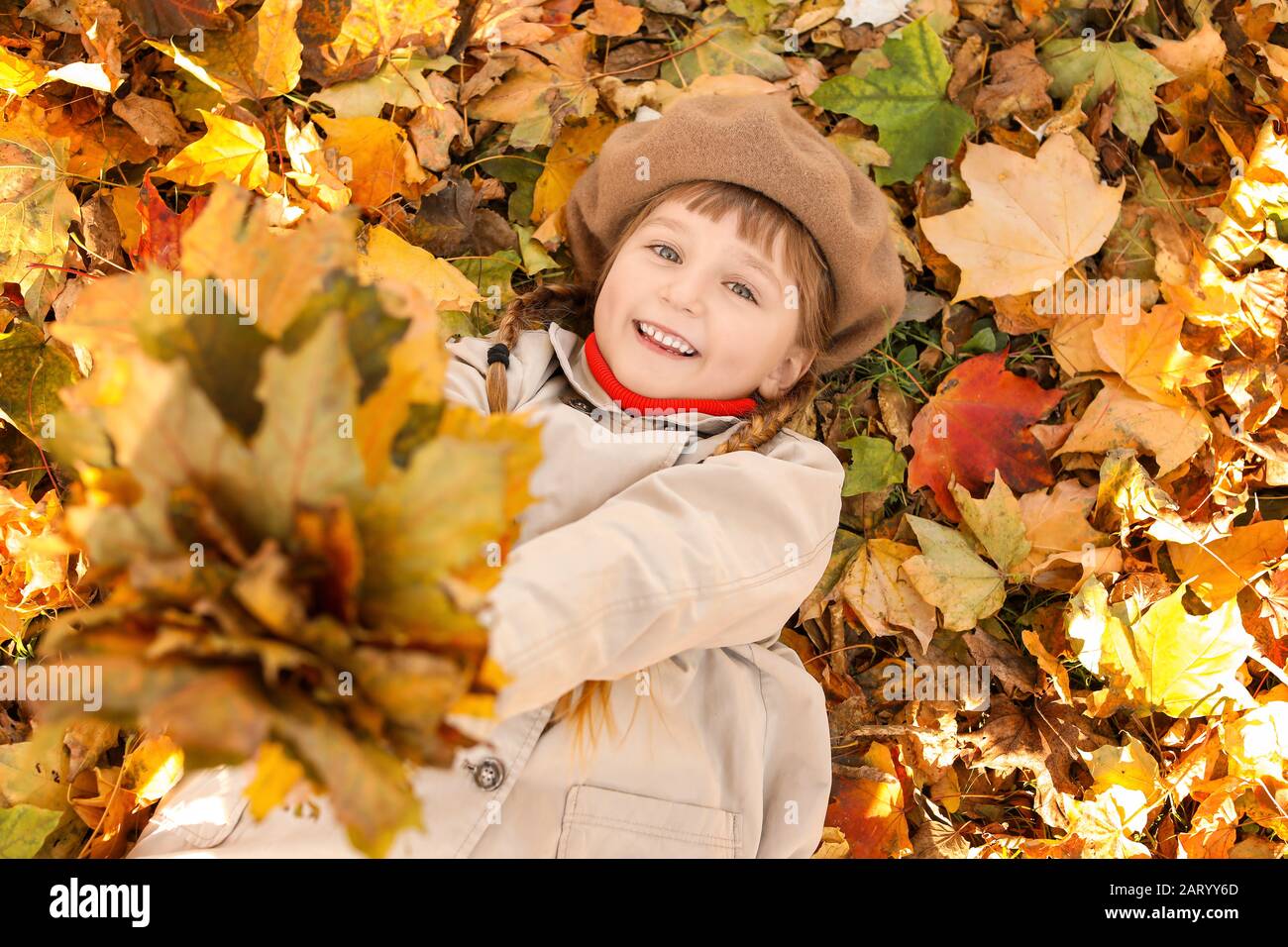 Cute little girl lying on leaves in autumn park Stock Photo - Alamy