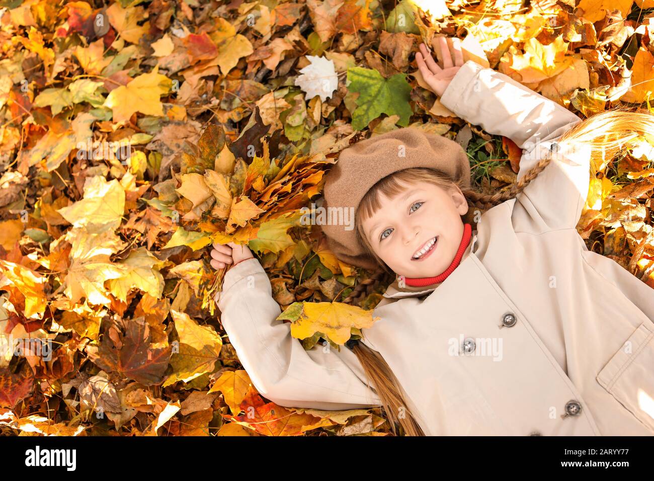 Cute little girl lying on leaves in autumn park Stock Photo - Alamy