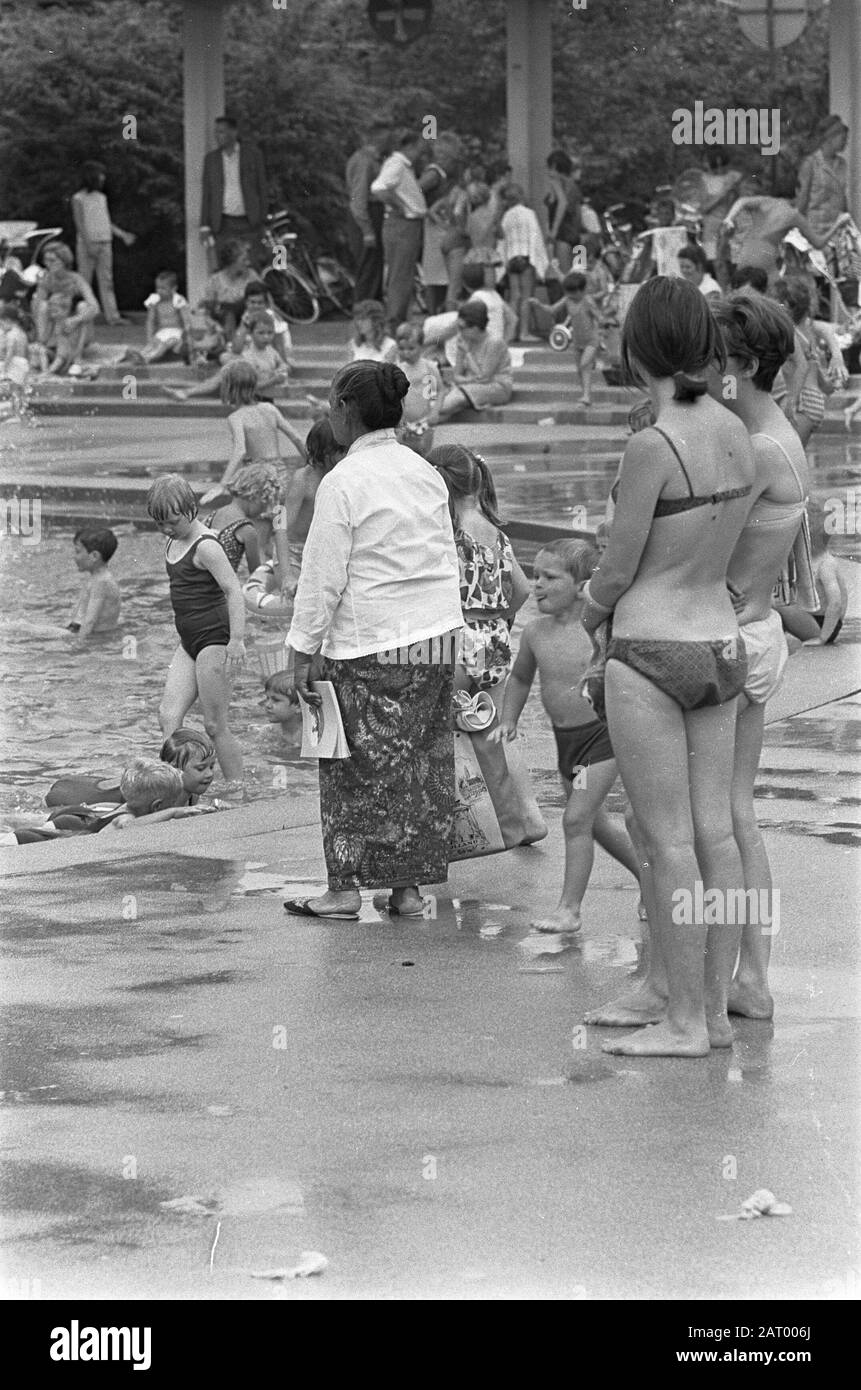 Woman in sarong and two women in bikini watching the children in the play  pond of