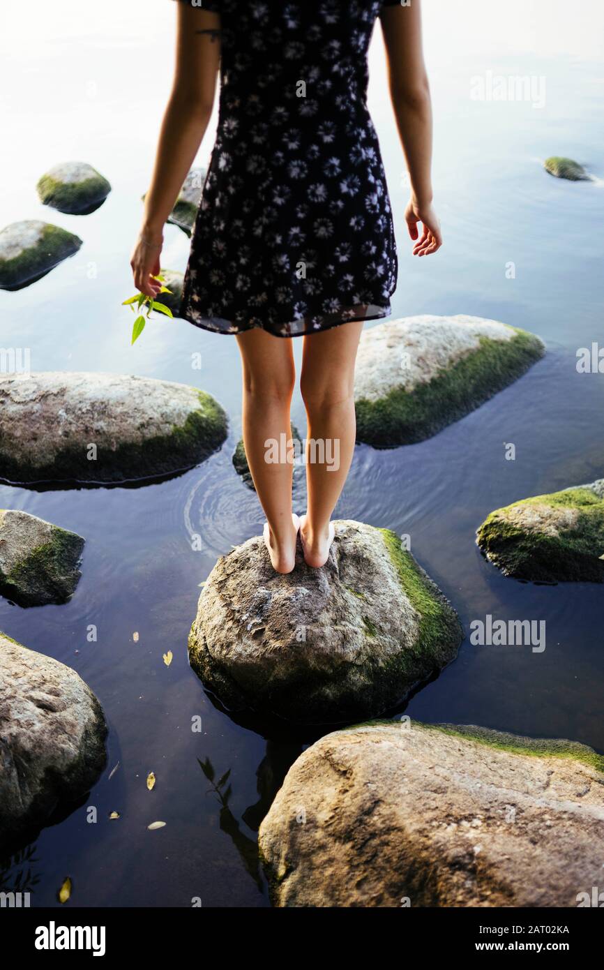 Barefoot woman standing on rock in sea Stock Photo