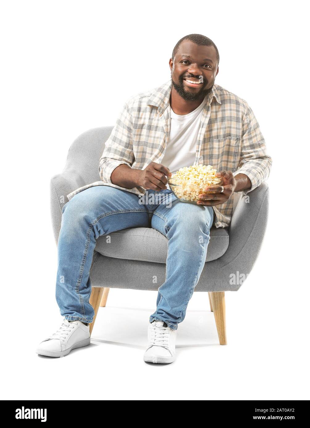 African-American man with popcorn watching TV while sitting in armchair  against white background Stock Photo - Alamy