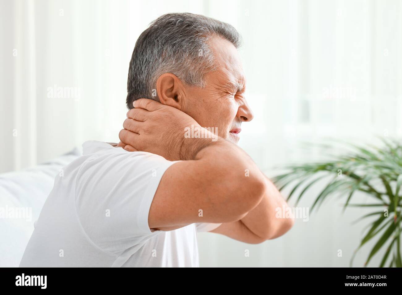 Mature man suffering from neck pain at home Stock Photo - Alamy
