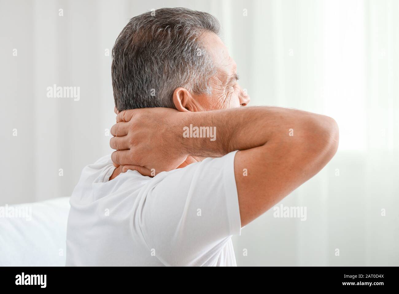 Mature man suffering from neck pain at home Stock Photo - Alamy