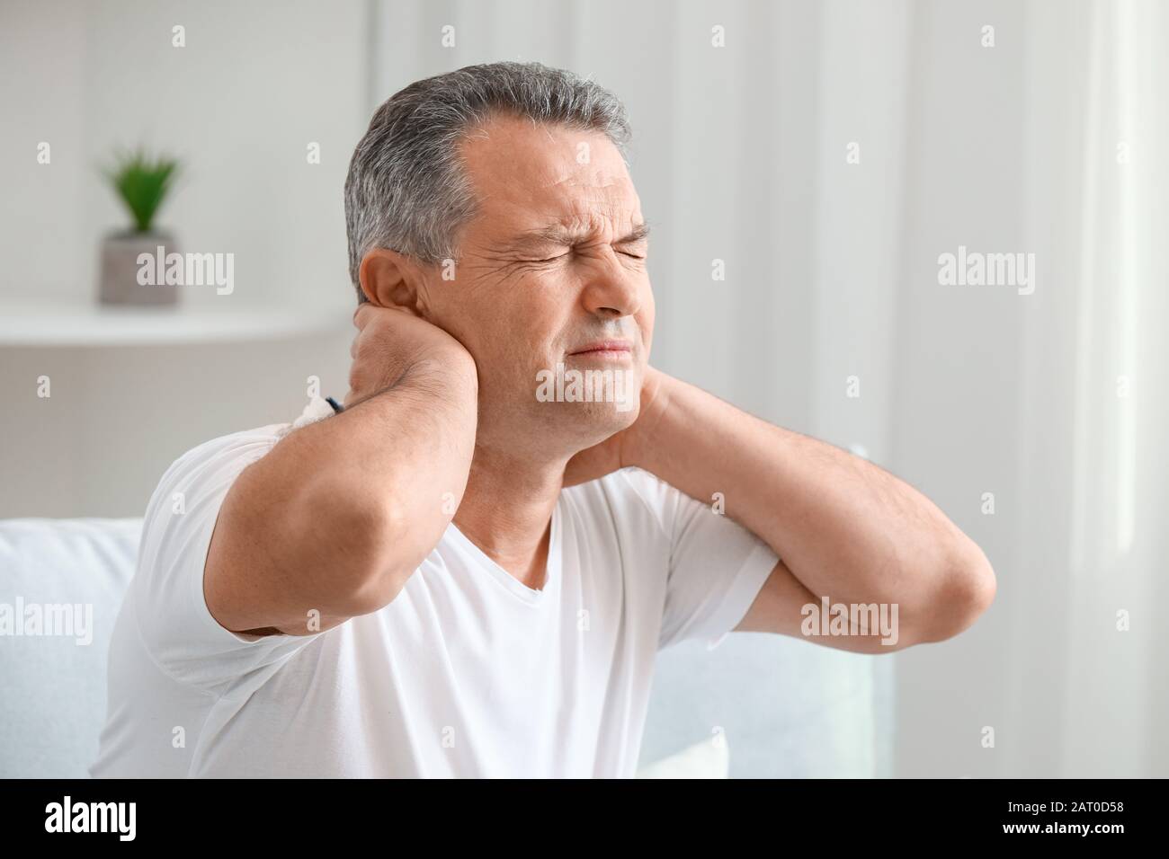 Mature man suffering from neck pain at home Stock Photo - Alamy