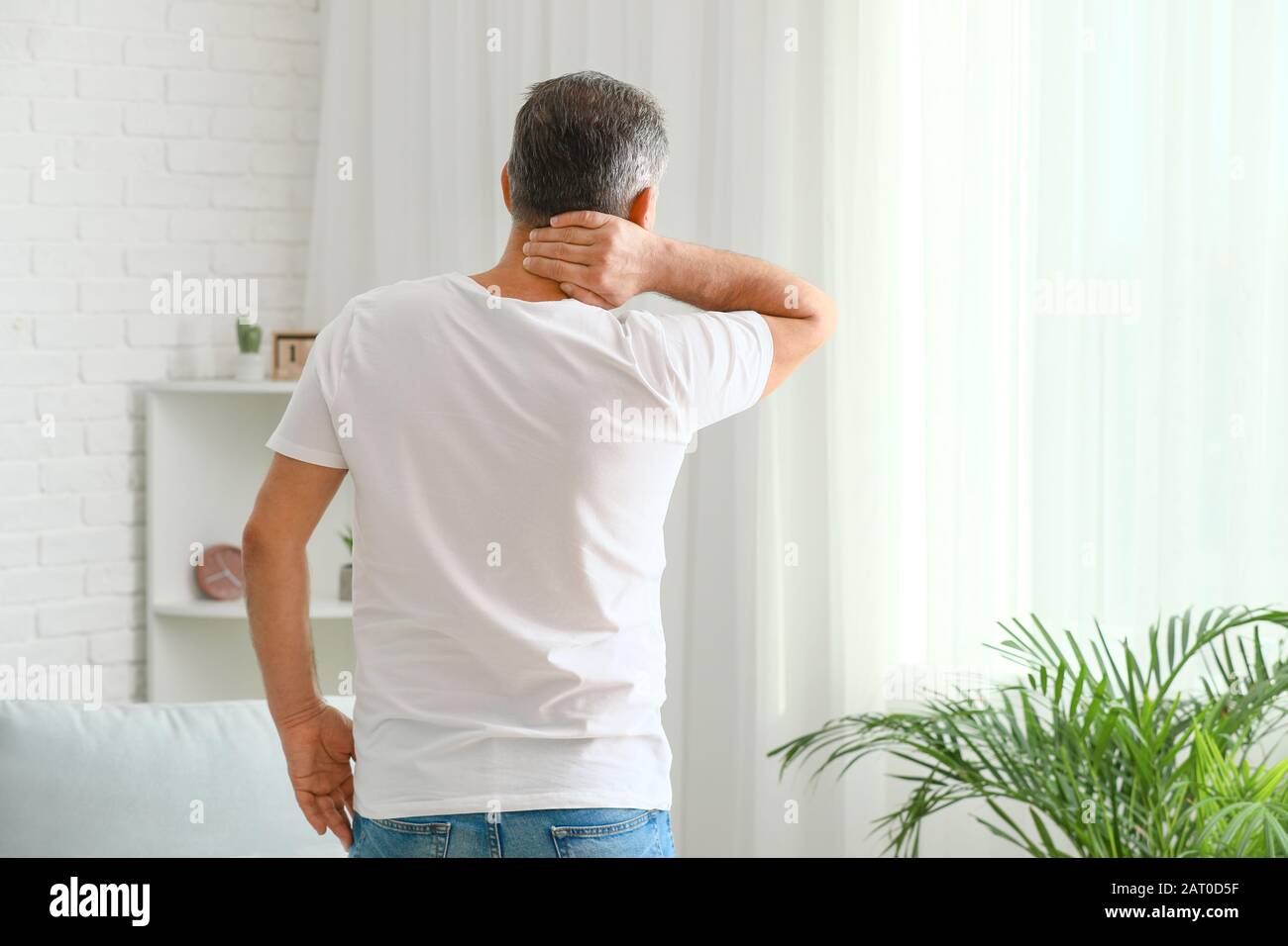 Mature man suffering from neck pain at home Stock Photo - Alamy