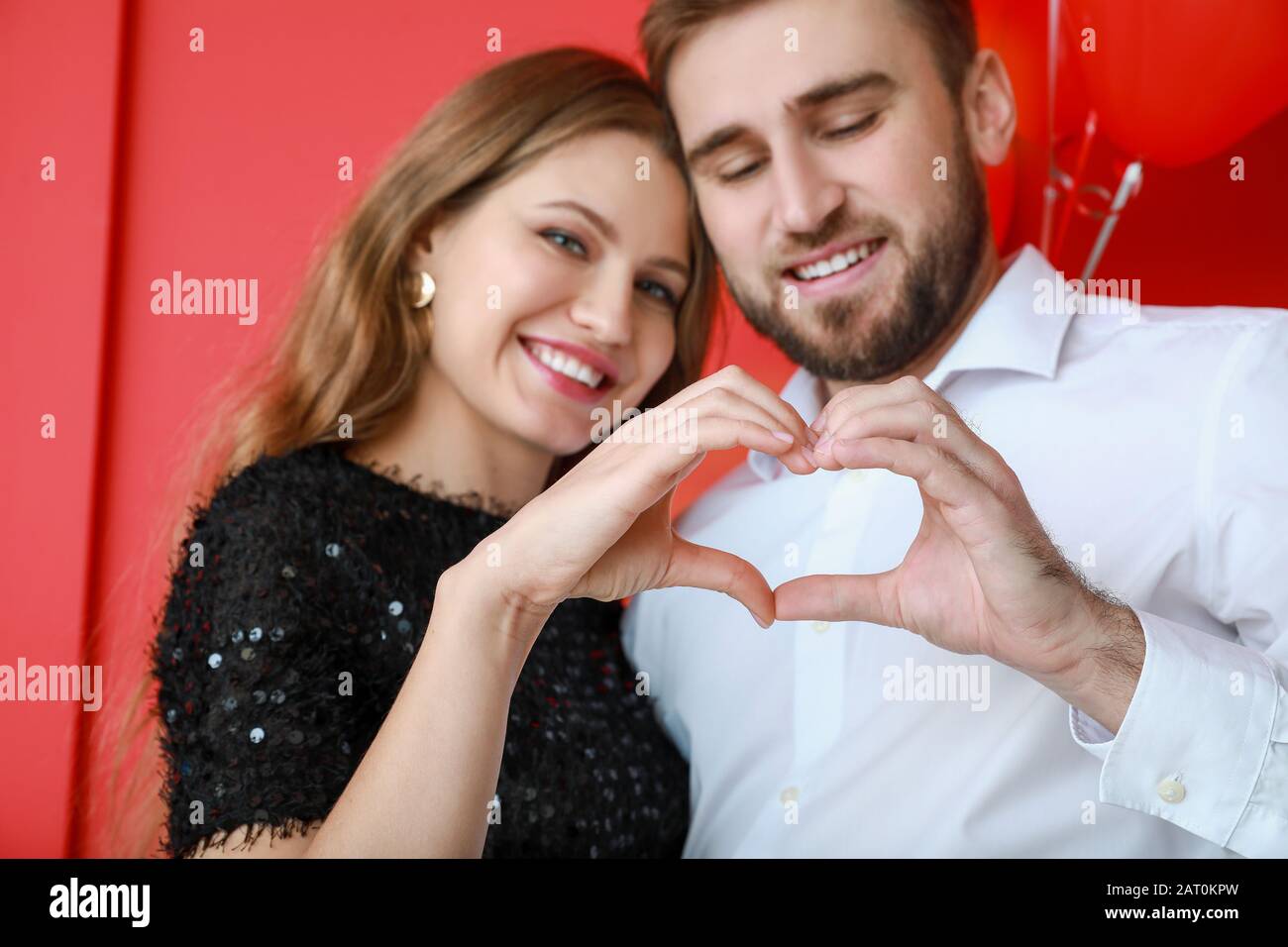 Happy young couple making heart with their hands on color background ...