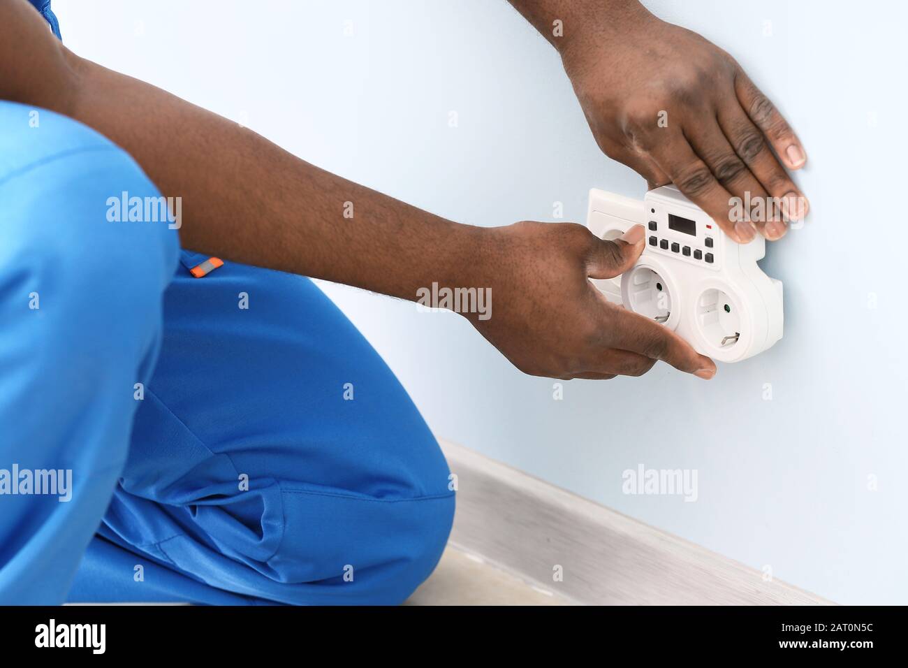 African-American electrician using socket voltage regulator in room Stock Photo