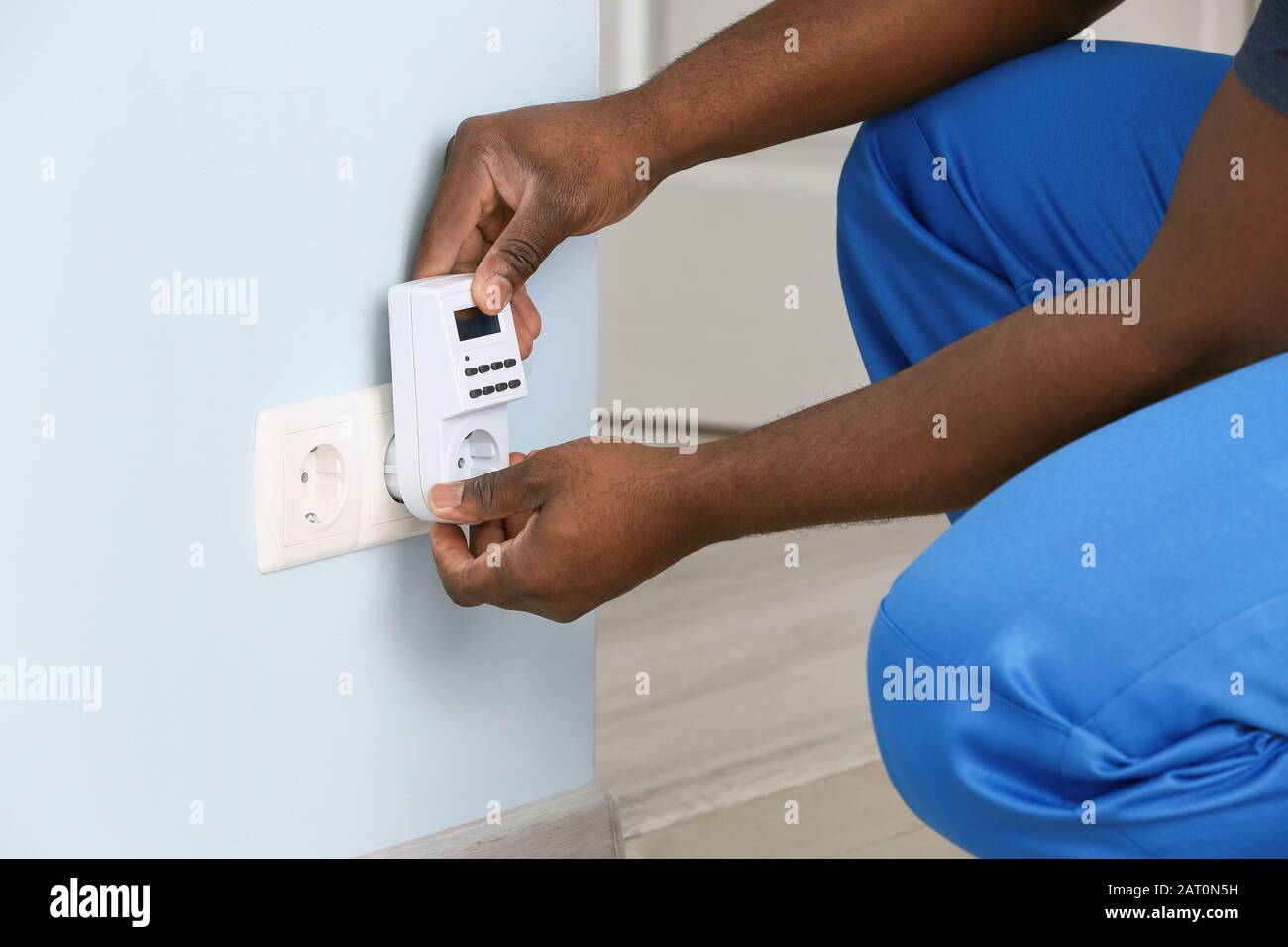African-American electrician using socket voltage regulator in room Stock Photo