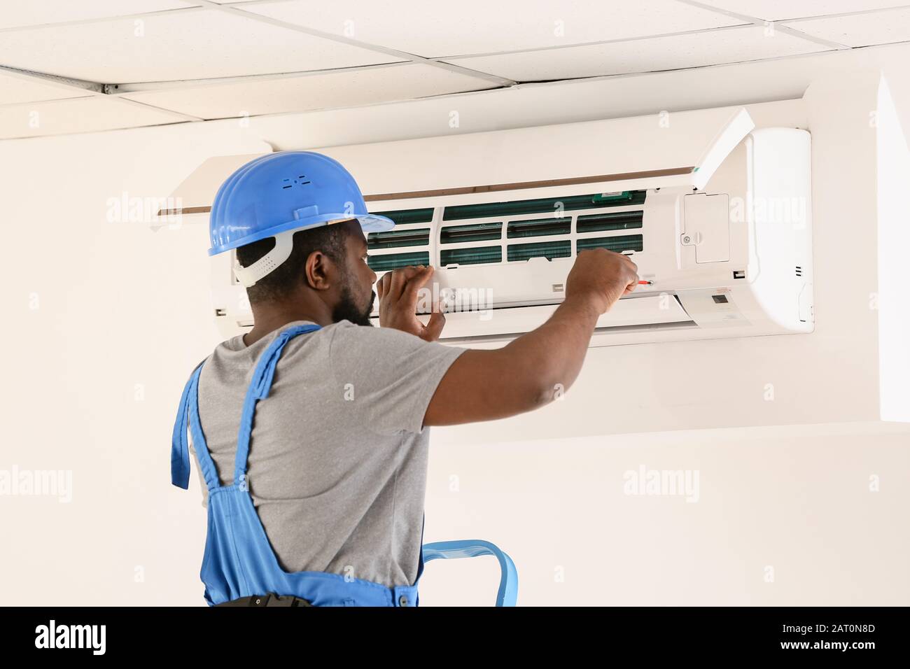 AfricanAmerican electrician repairing air conditioner indoors Stock