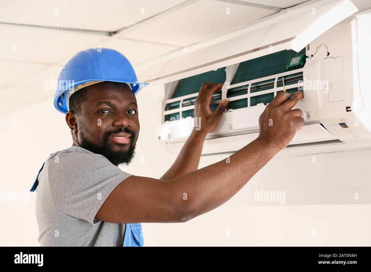 AfricanAmerican electrician repairing air conditioner indoors Stock