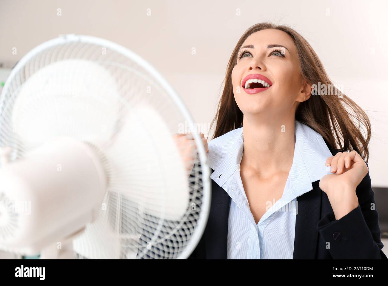 Young woman using electric fan during heatwave in office Stock Photo ...