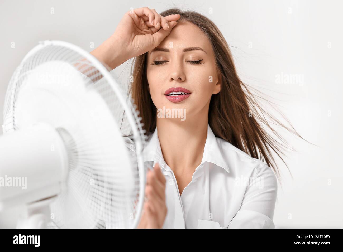 Young woman using electric fan during heatwave in office Stock Photo ...