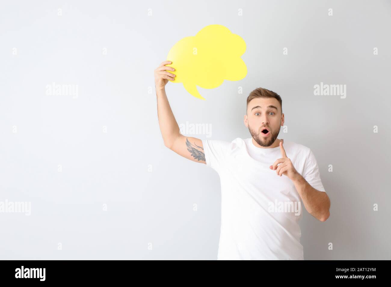 Surprised young man with blank speech bubble on light background Stock Photo