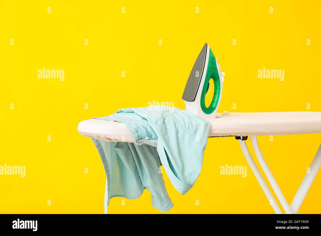 Iron and clean clothes on board against color background Stock Photo