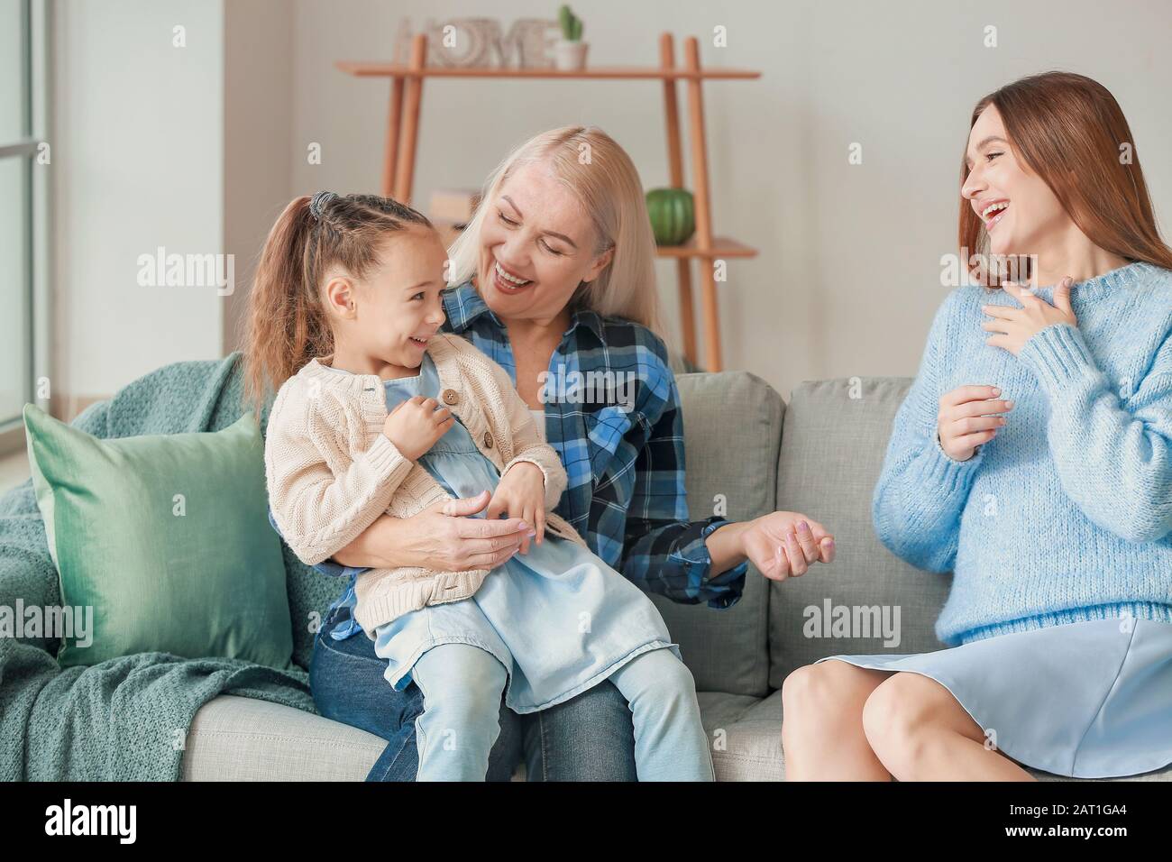 Young woman with her little daughter and mother spending time together at home Stock Photo