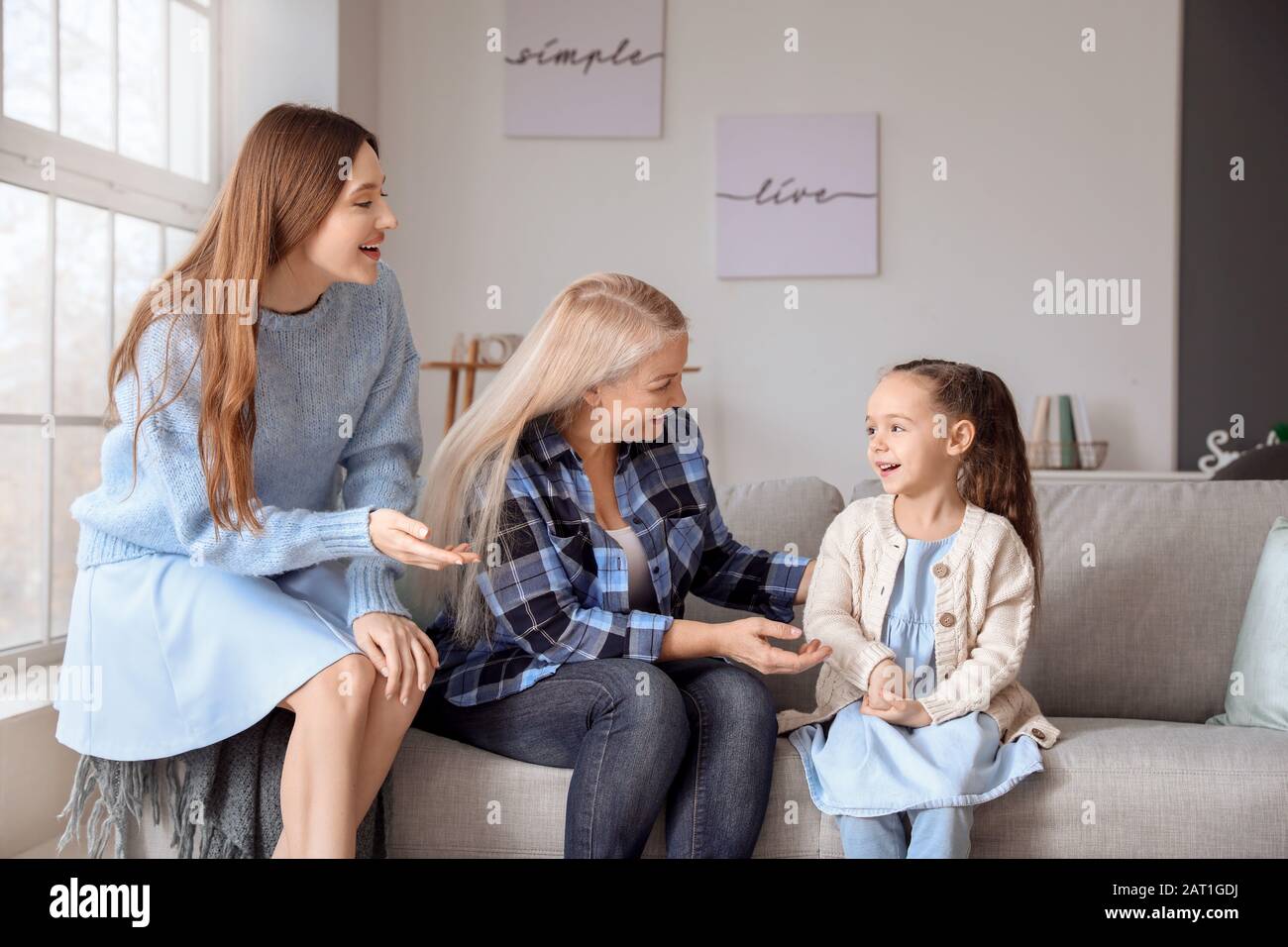 Young woman with her little daughter and mother spending time together at home Stock Photo