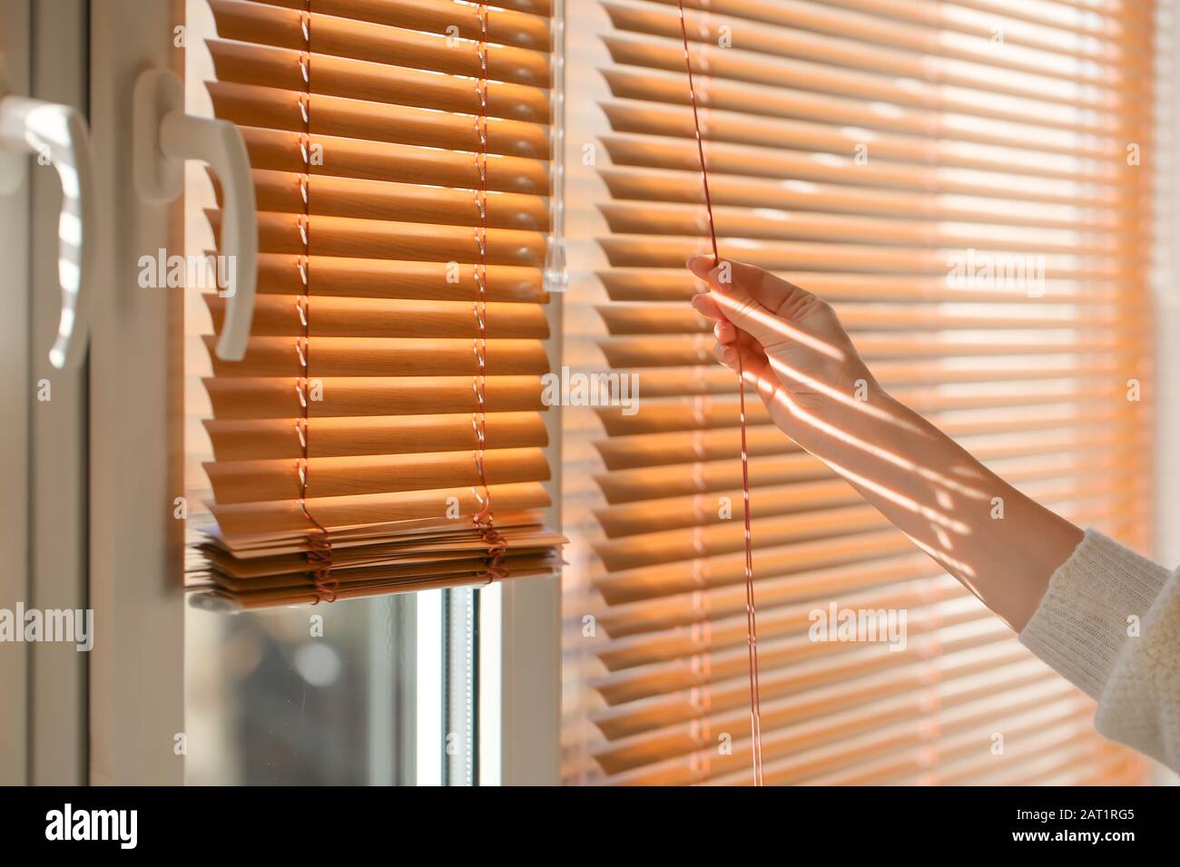 Woman opening blinds on window Stock Photo