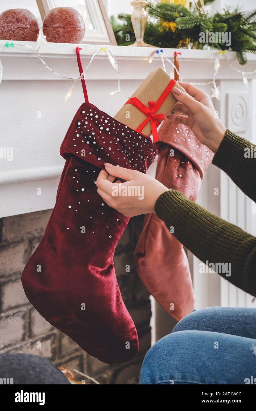 Woman putting gifts into Christmas socks hanging on fireplace at home Stock Photo