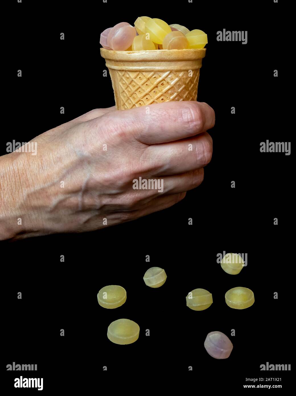 Woman hand holds up a cone full of fruit candies on a black background Stock Photo