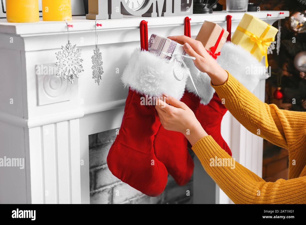 Woman putting gifts into Christmas socks hanging on fireplace at home Stock Photo