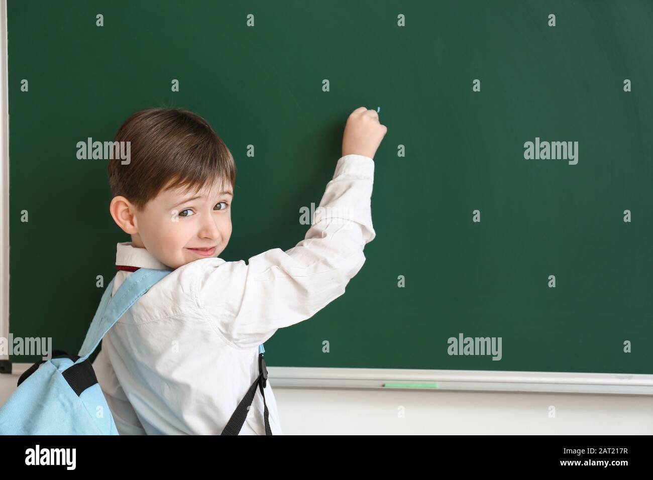 Little schoolboy writing on blackboard in classroom Stock Photo - Alamy