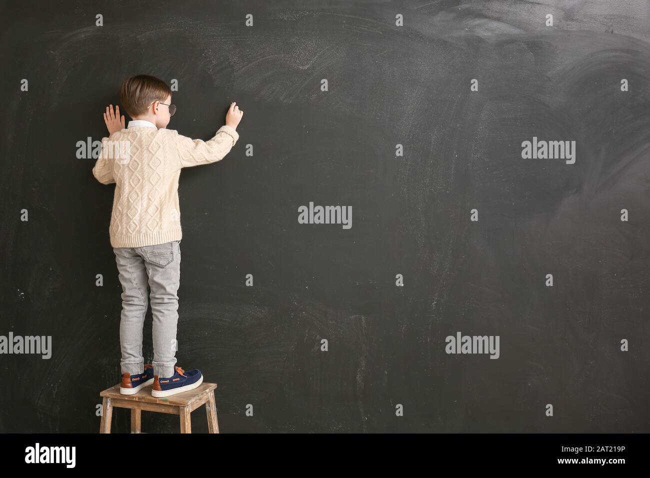Little schoolboy writing on blackboard in classroom Stock Photo - Alamy