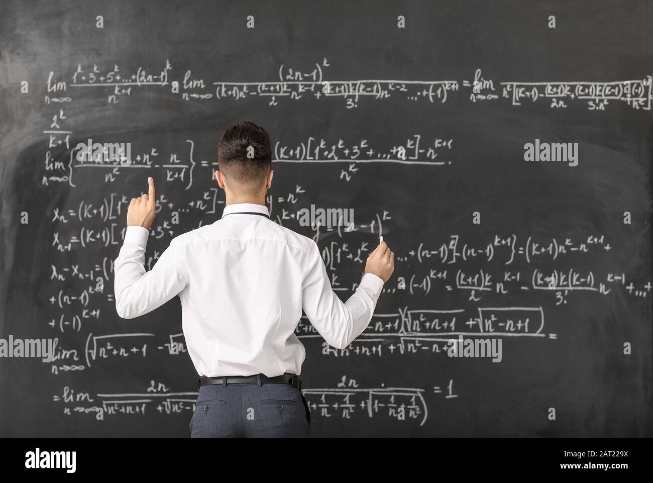 Male teacher with raised index finger near blackboard in classroom Stock Photo