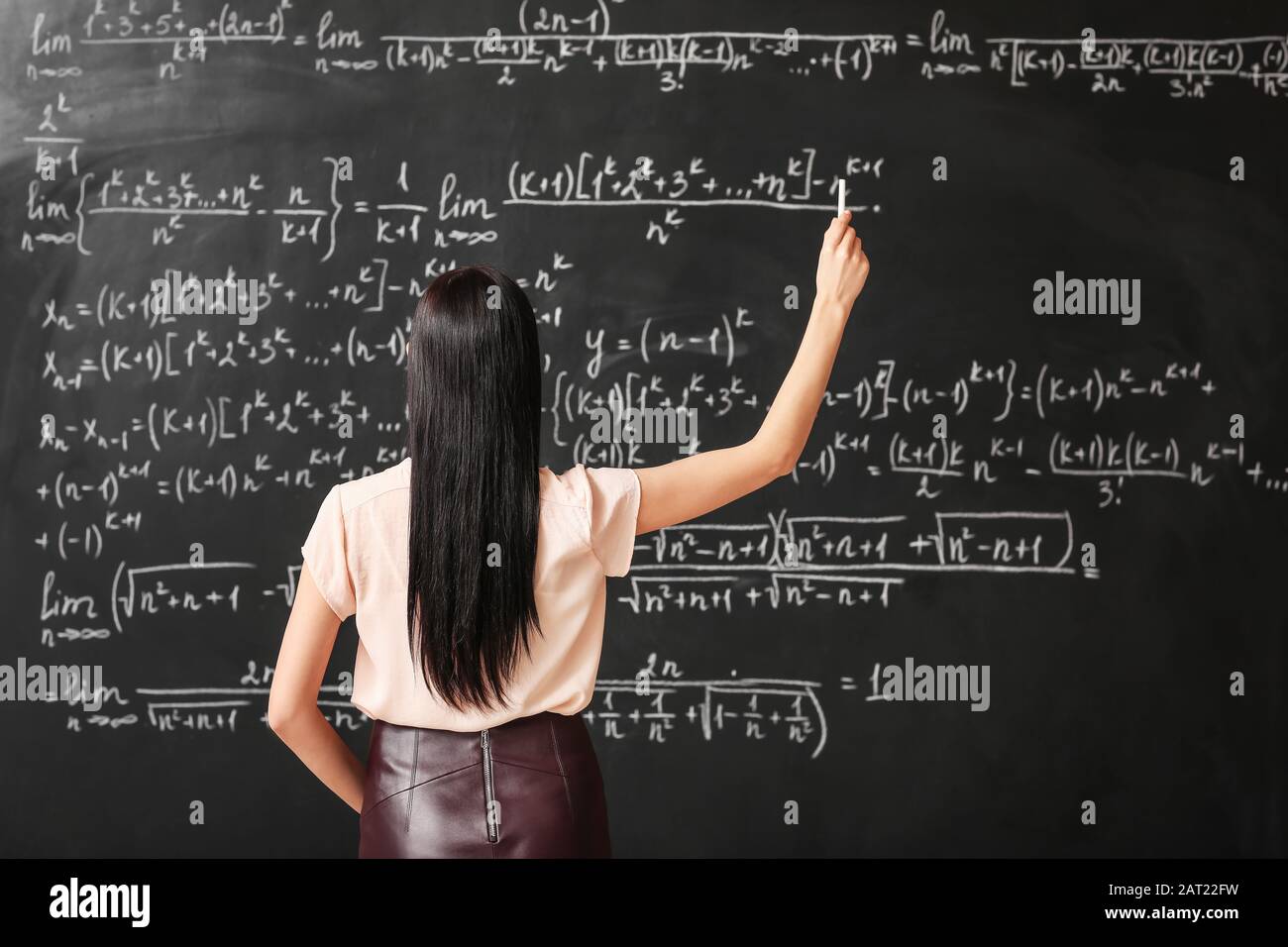 Female teacher writing on blackboard in classroom Stock Photo