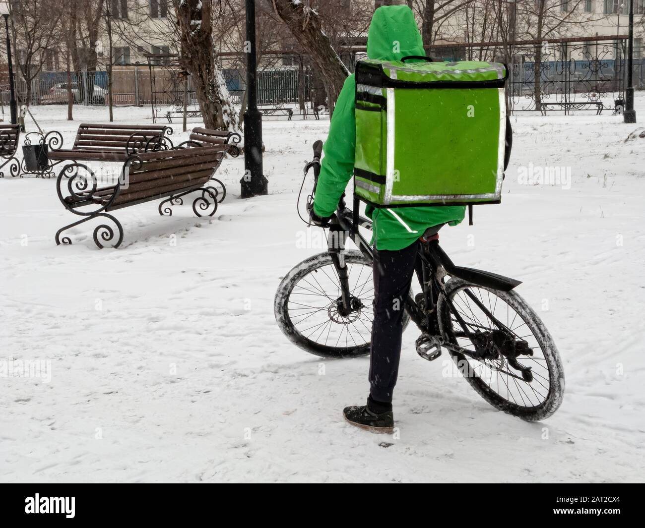 24-hour delivery service from cafes and restaurants. Take-away courier on a bike with a green isothermal backpack rides fast. Courier delivers food by Stock Photo