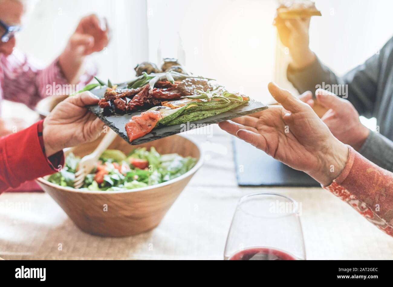 Senior people having italian vegan vegetarian lunch at home - Mature friends eating bbq vegetables,fresh salads and toasting red wine - Healthy concep Stock Photo