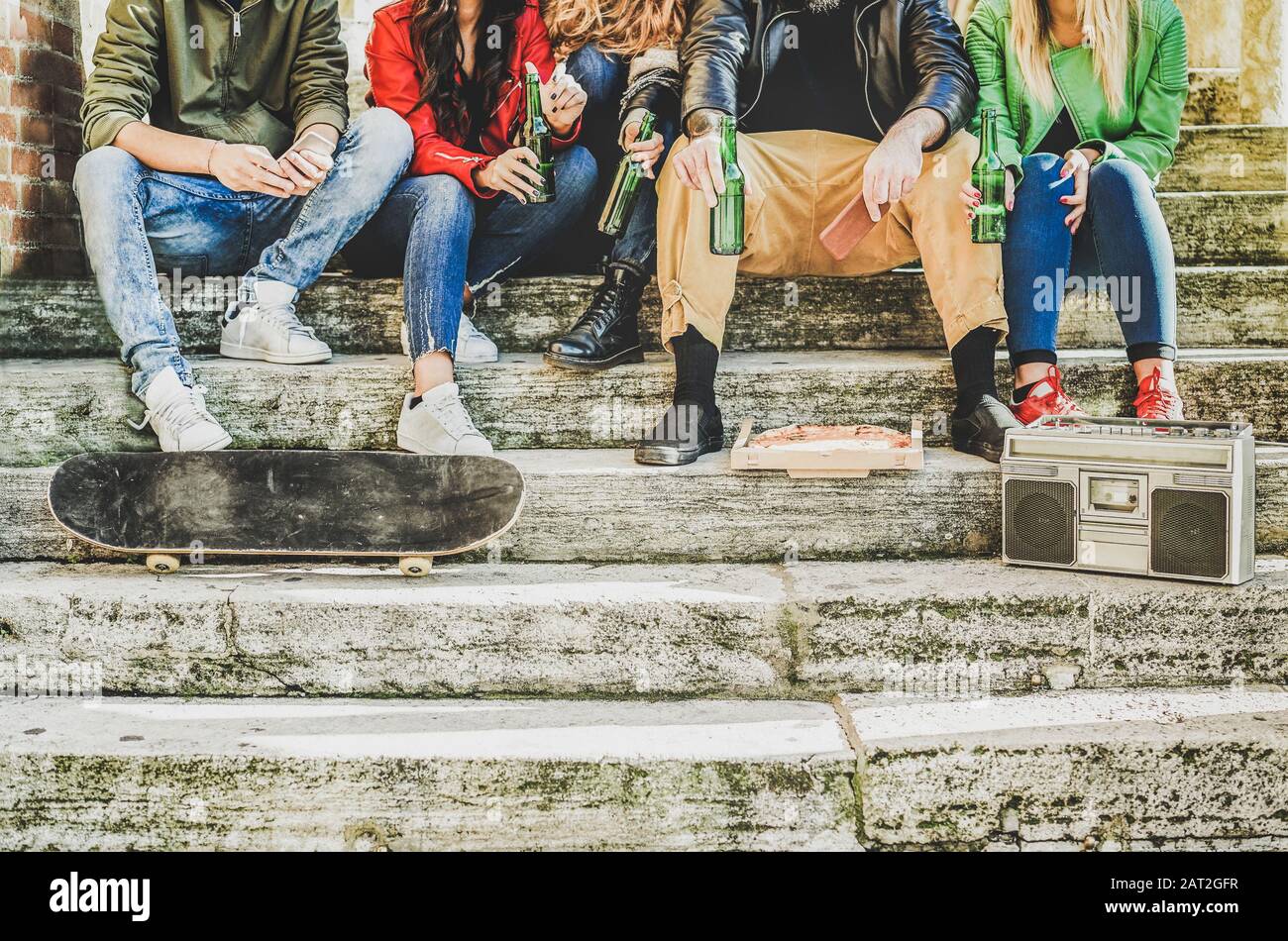 Group of friends drinking beer and eating takeout pizza outdoor -Young people sitting in staircase having fun listening music - Friendship, party, soc Stock Photo