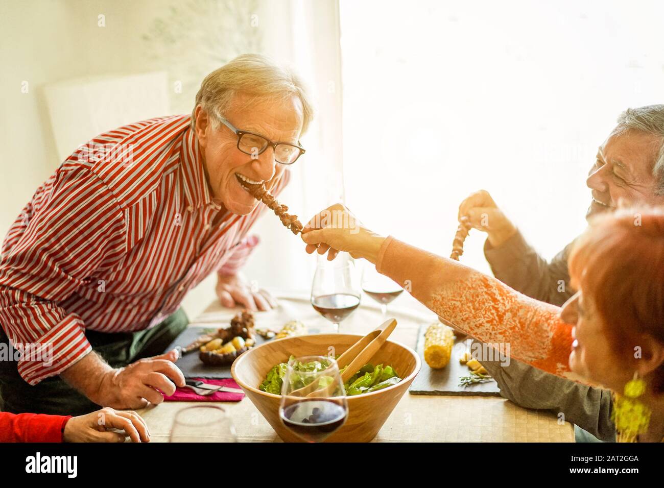 Happy senior friends having barbecue lunch at home - Old people having fun eating tasty meat skewers at bbq meal - Joyful elderly active lifestyle con Stock Photo
