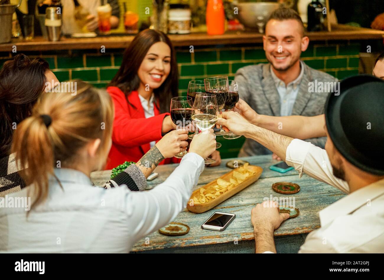 Happy friends raising glasses for cheering and toasting wine in trendy cocktail bar restaurant - Young people enjoying apres before dinner - Focus on Stock Photo