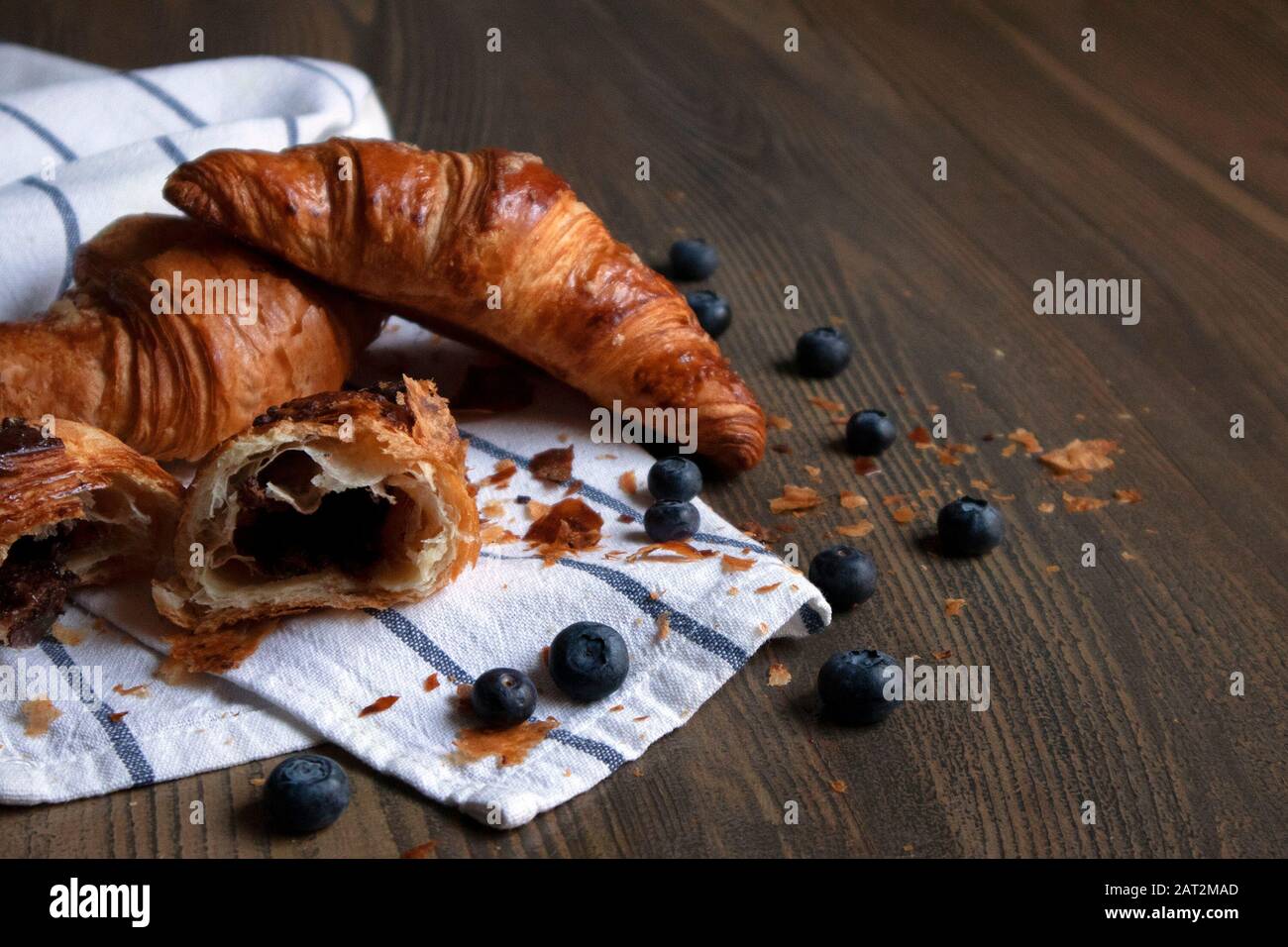 Few appetizing ruddy croissants with filling and blueberries lying on a striped towel against wooden table Stock Photo