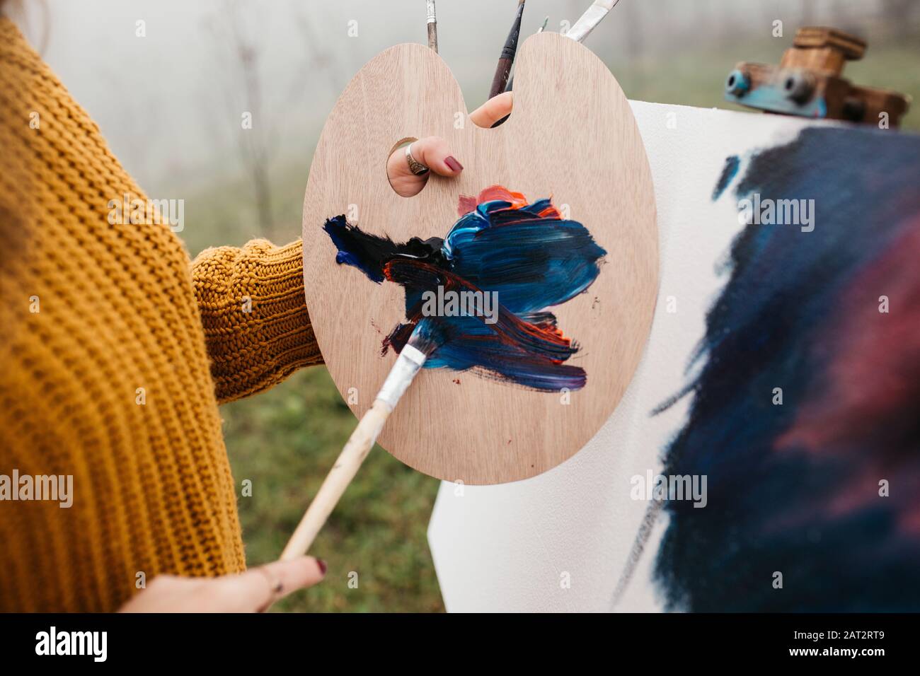 Close up photo of young female artist working on painting outdoors. She
