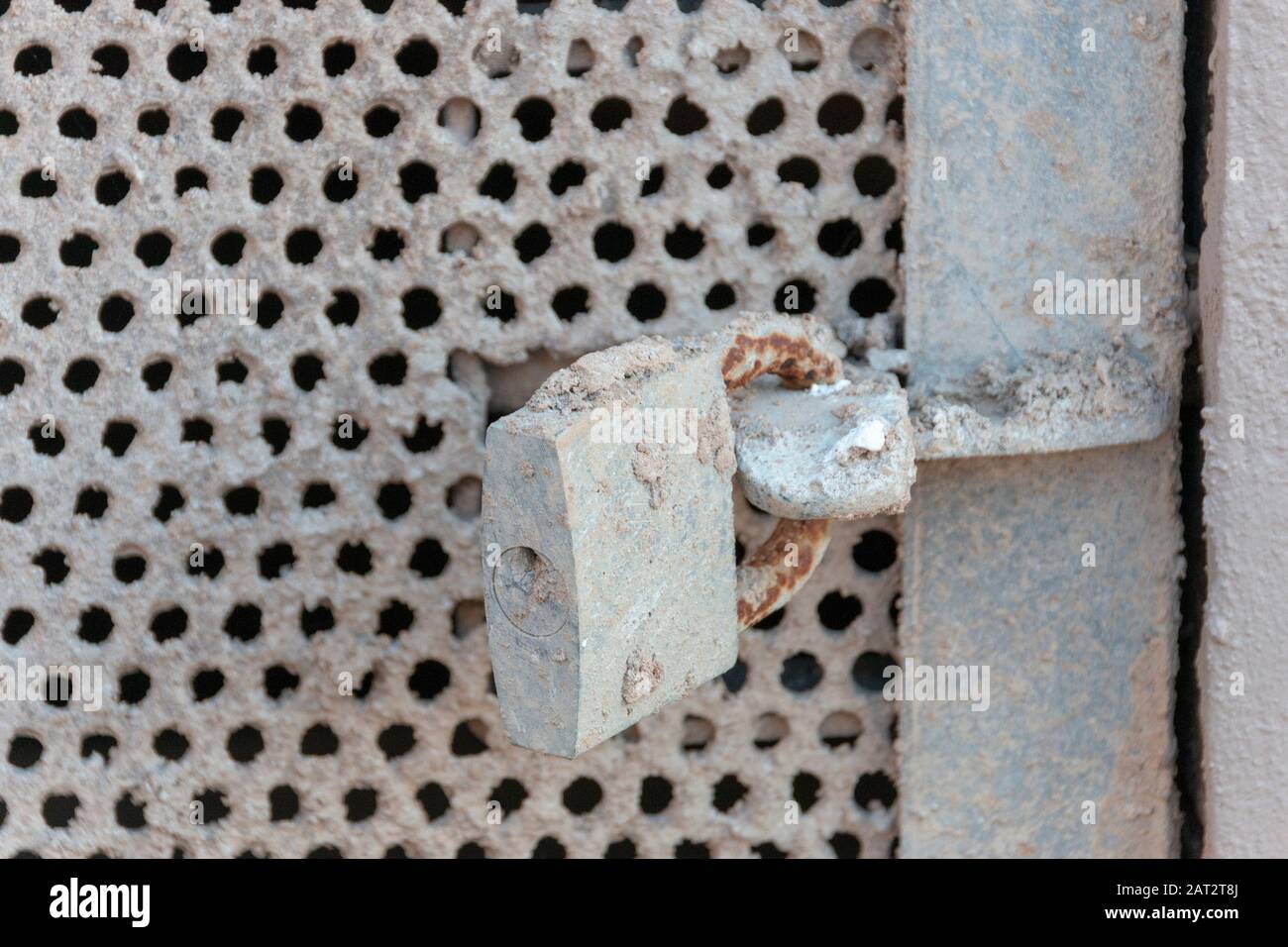 A close up view of a locked metal meshed door leading to a passway under a building. Covered in concrete Stock Photo