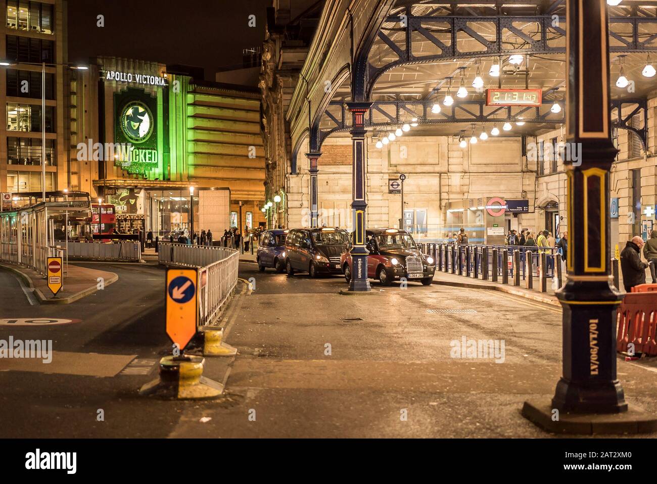 Urban street scene outside main entrance of London Victoria Station at night. View of London taxis queuing & stage musical Wicked at Apollo Victoria. Stock Photo
