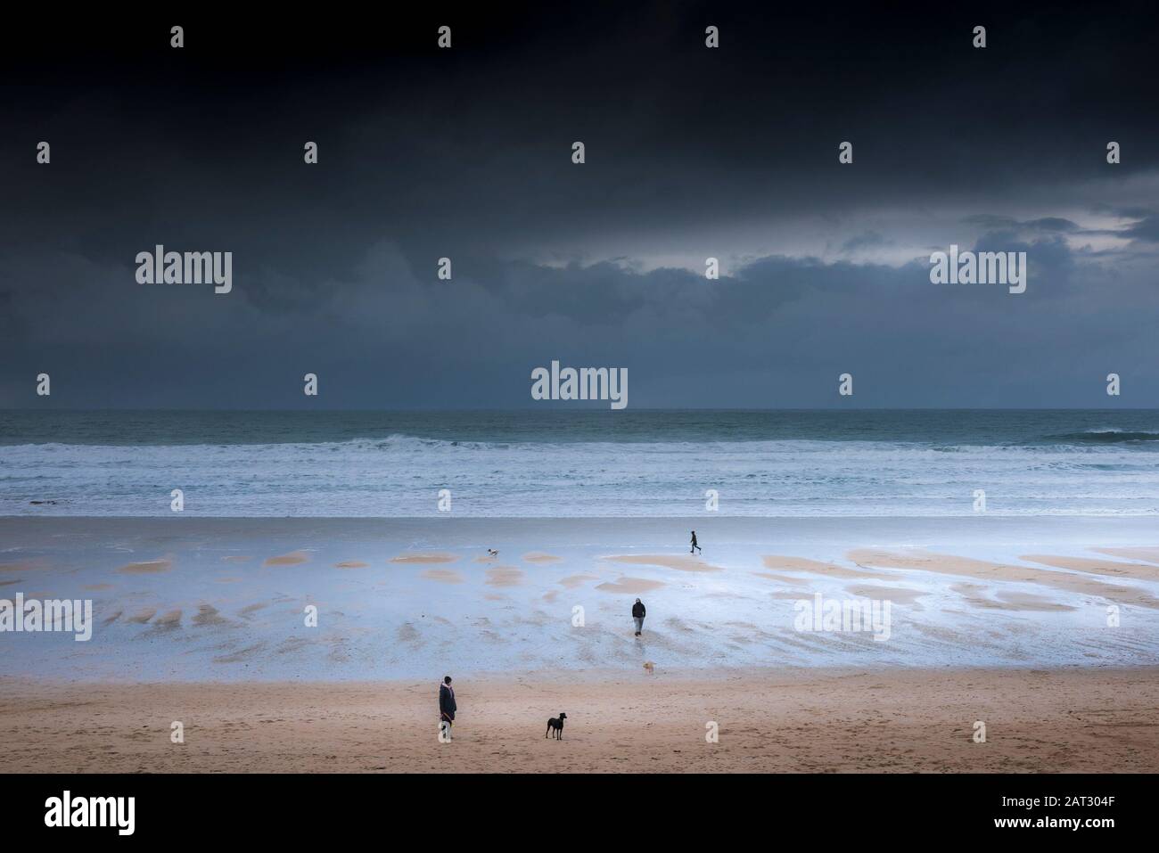 Dog walkers and their pets on Fistral beach as dark rain clouds approach Newquay in Cornwall. Stock Photo