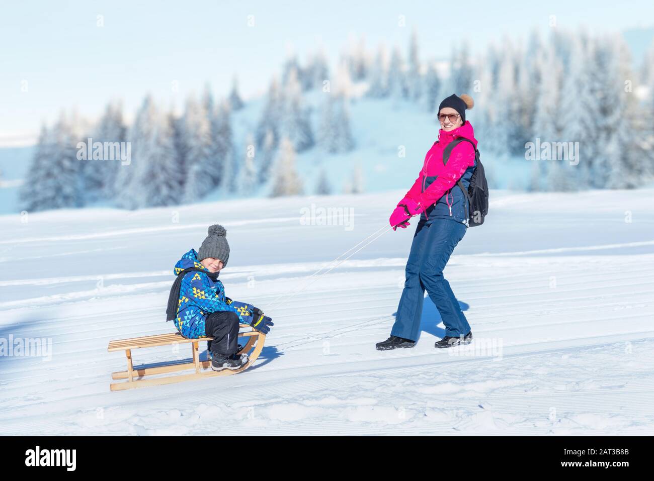 Mother dragging the snow sled with boy. Mountain in background. Concept od keep children healthy during the winter Stock Photo