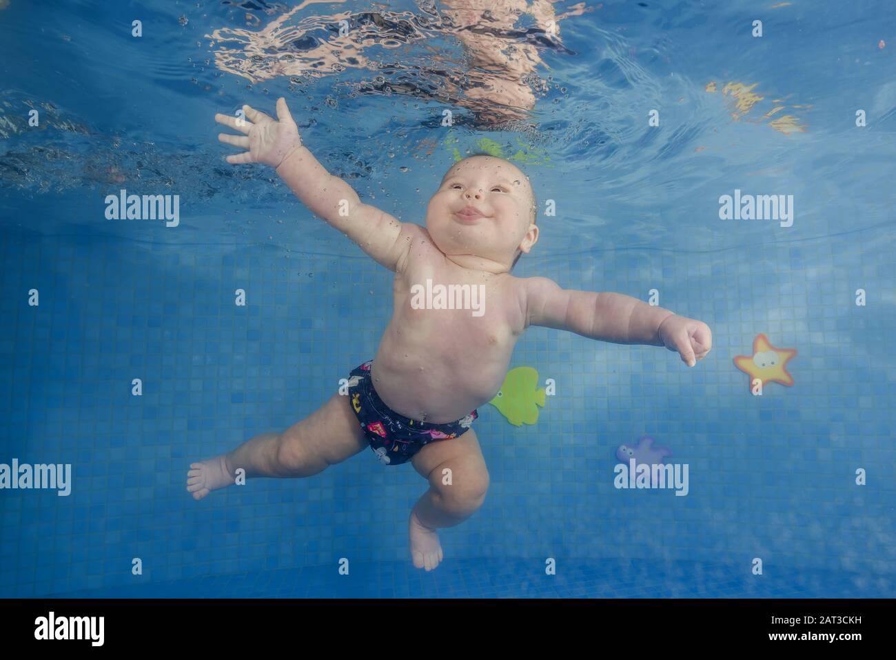 Little baby girl learns to swims underwater. Baby swimming underwater in the pool on a blue water background. Stock Photo