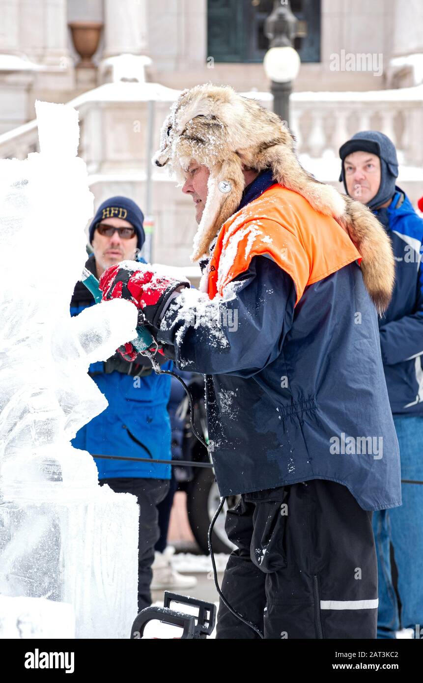 St. Paul, MN/USA - January 25, 2020: Ice sculptor at multi-block ice carving competition shaping ice while spectators gather during annual winter carn Stock Photo