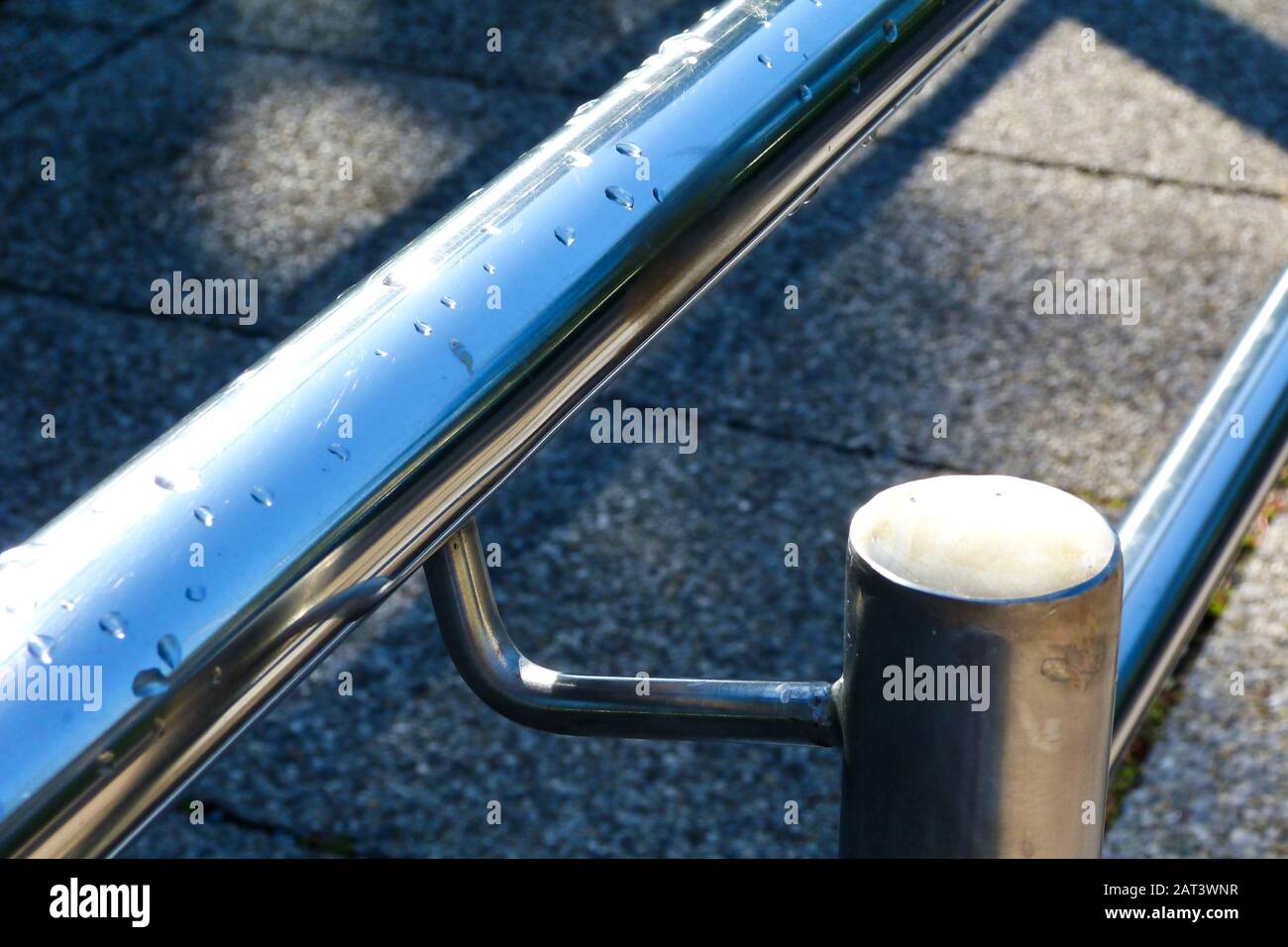concrete tile paved wheelchair and handicap ramp. stainless steel handrail in selective focus. blurry gray background. barrier free access concept. Stock Photo