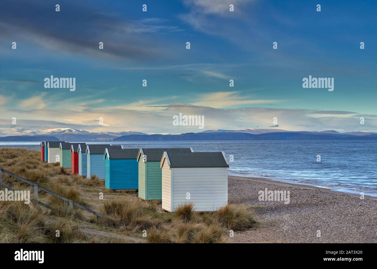 FINDHORN BEACH MORAY SCOTLAND A ROW OF COLOURED BEACH HUTS OR CHALETS A BLUE SKY AND SEA THE BLACK ISLE IN THE DISTANCE Stock Photo