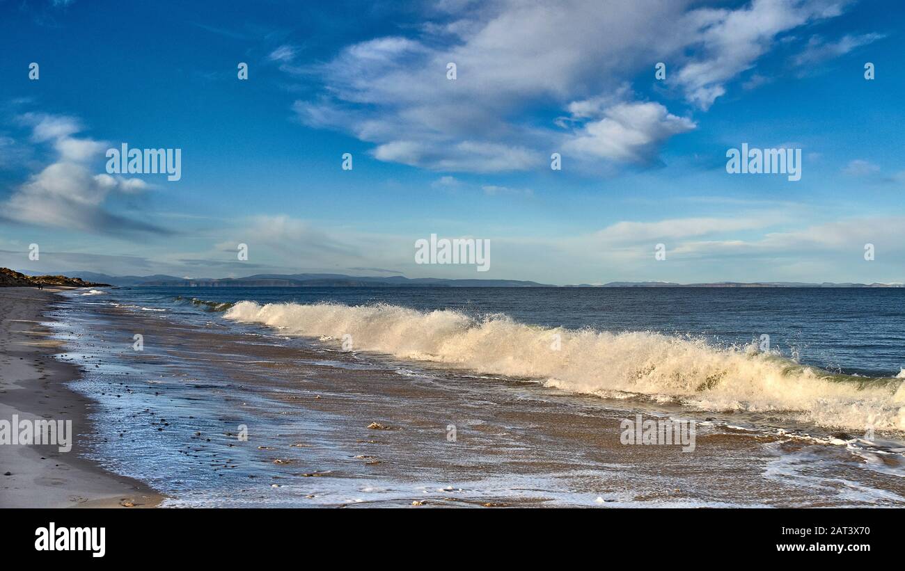 FINDHORN BEACH MORAY SCOTLAND SANDY BEACH BLUE SKY SEA AND A LARGE BREAKING WAVE AND WHITE SURF Stock Photo