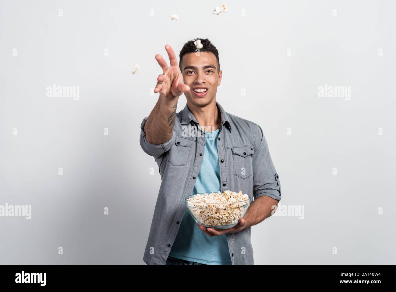 Mulatto man holding a plate of popcorn in his hands and throwing popcorn at the camera Stock Photo