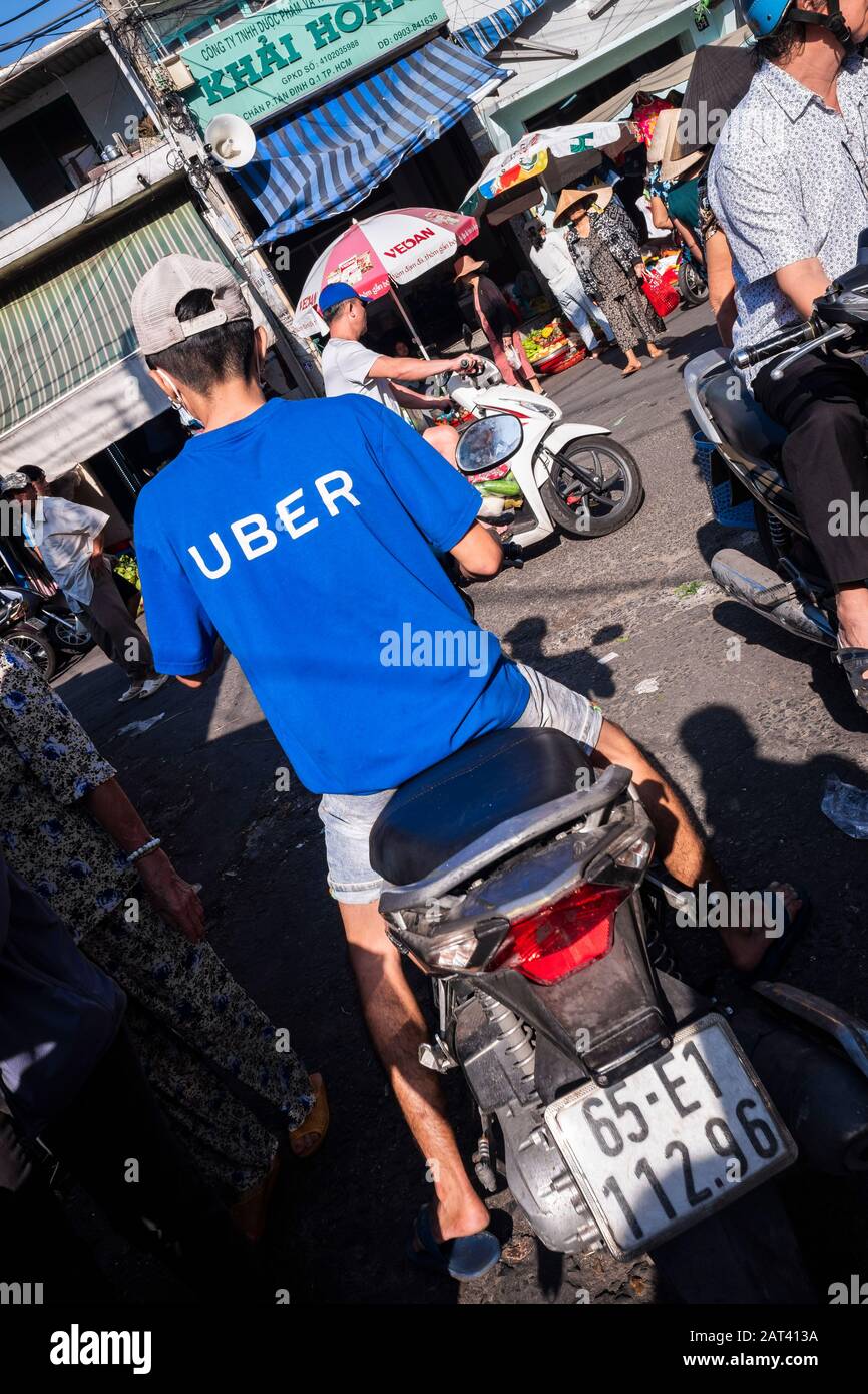 Man wearing Uber tee shirt driving through street market, Ho Chi Minh City, Vietnam Stock Photo