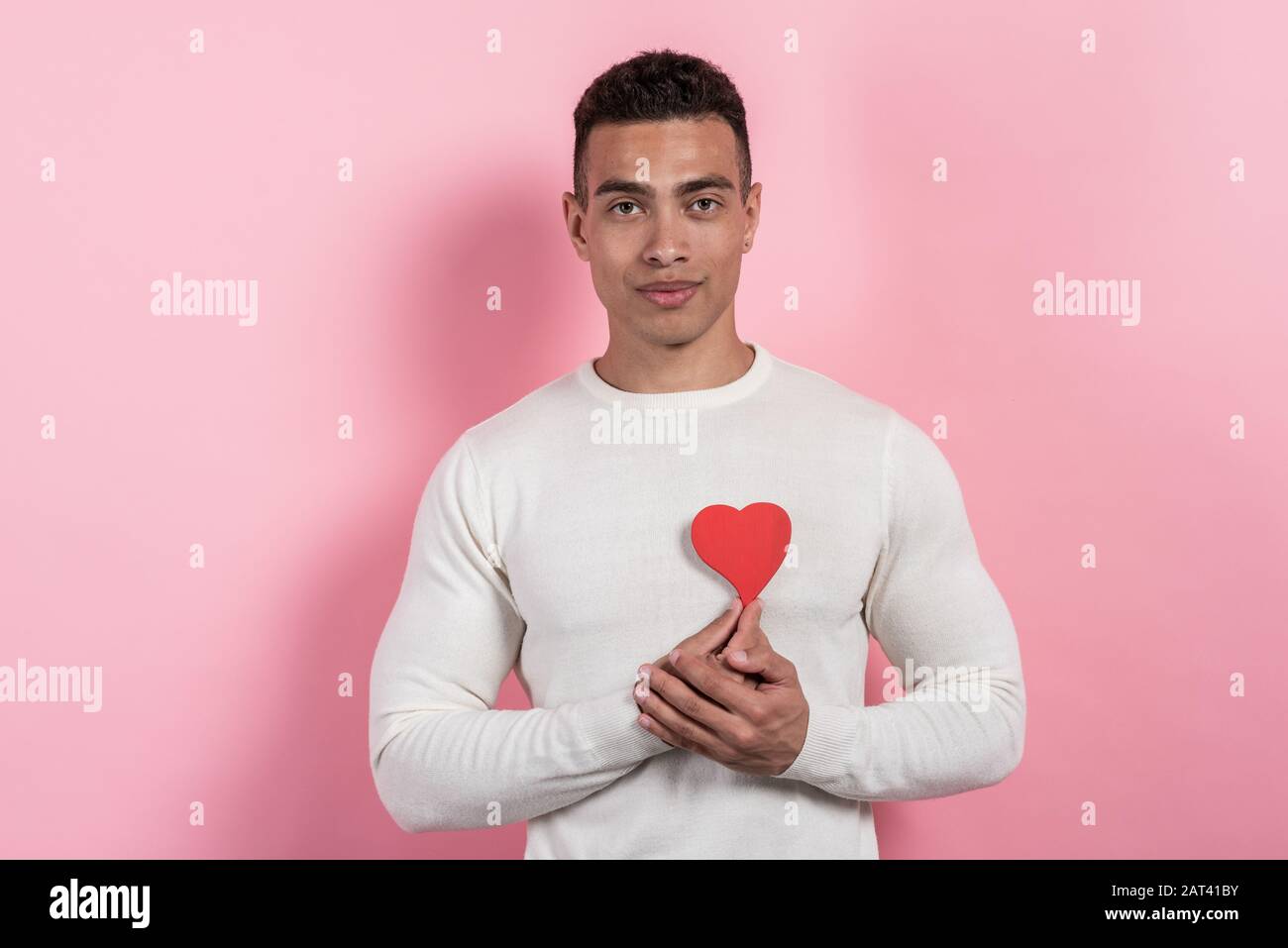 Young pretty mulatto man holding a heart-object and   embosom it, learned to his chest Stock Photo