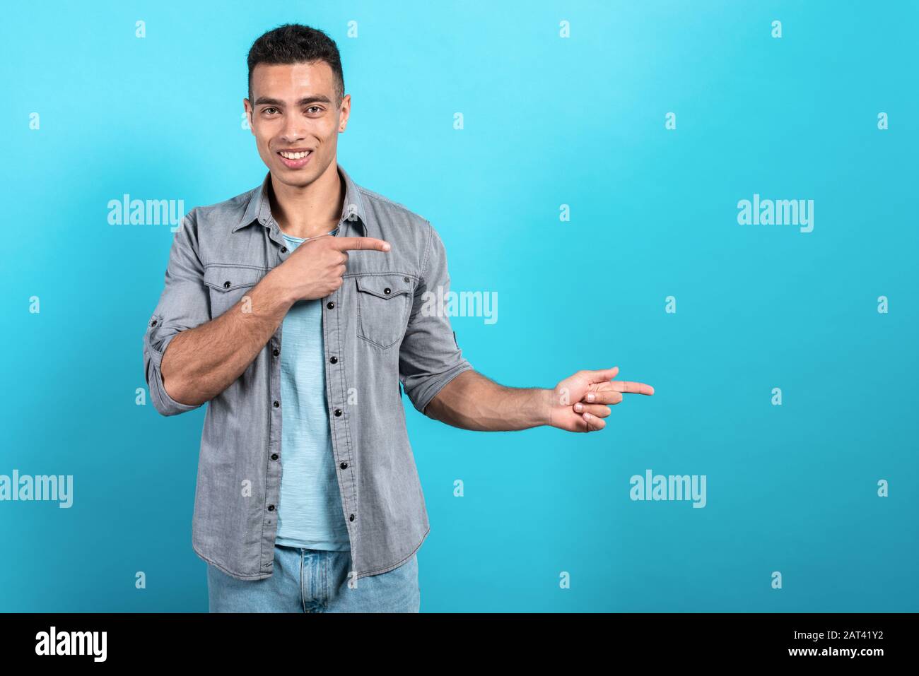 Happy mulatto  man smiling and pointing sideaway makes gesture from his fingers- Image Stock Photo
